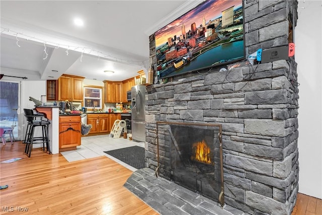 living room featuring crown molding, a stone fireplace, sink, and light hardwood / wood-style flooring