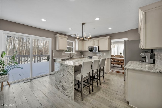 kitchen featuring pendant lighting, a center island, light hardwood / wood-style floors, light stone counters, and a chandelier