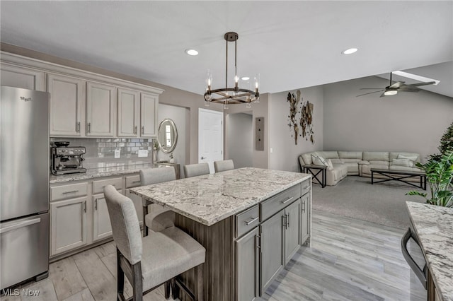 kitchen with stainless steel fridge, ceiling fan with notable chandelier, light hardwood / wood-style flooring, a center island, and a breakfast bar area