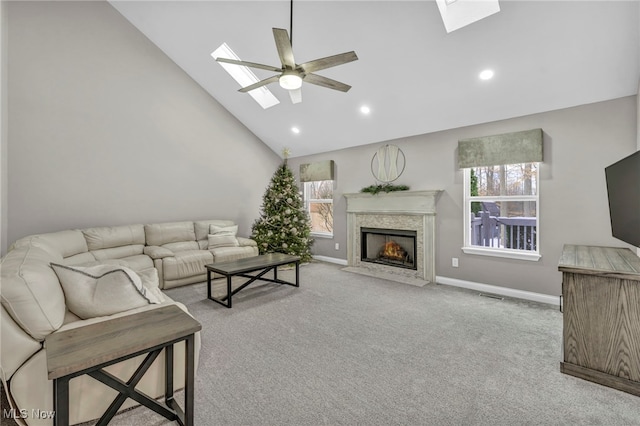 carpeted living room with a skylight, ceiling fan, a fireplace, and high vaulted ceiling