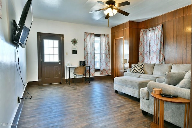 living room with dark hardwood / wood-style flooring, ceiling fan, and wooden walls