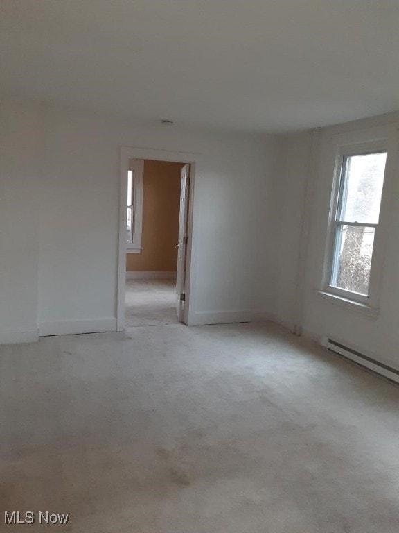 carpeted empty room featuring a baseboard heating unit