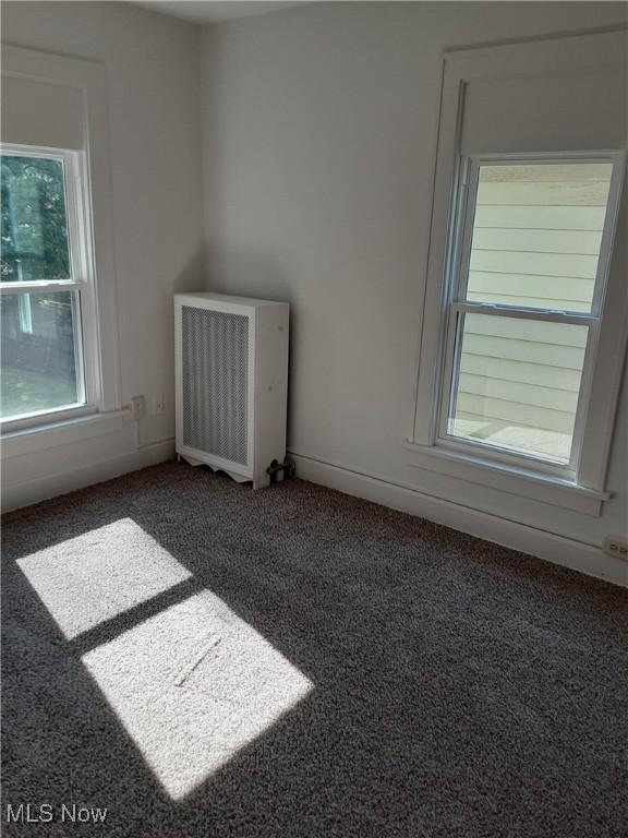 unfurnished room featuring dark colored carpet and radiator heating unit