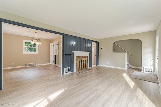 unfurnished living room with a notable chandelier, light hardwood / wood-style floors, and a brick fireplace