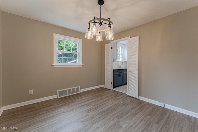 unfurnished dining area with light hardwood / wood-style floors, a notable chandelier, and sink