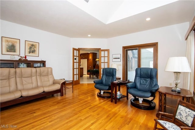 living room with a skylight, french doors, and light hardwood / wood-style flooring