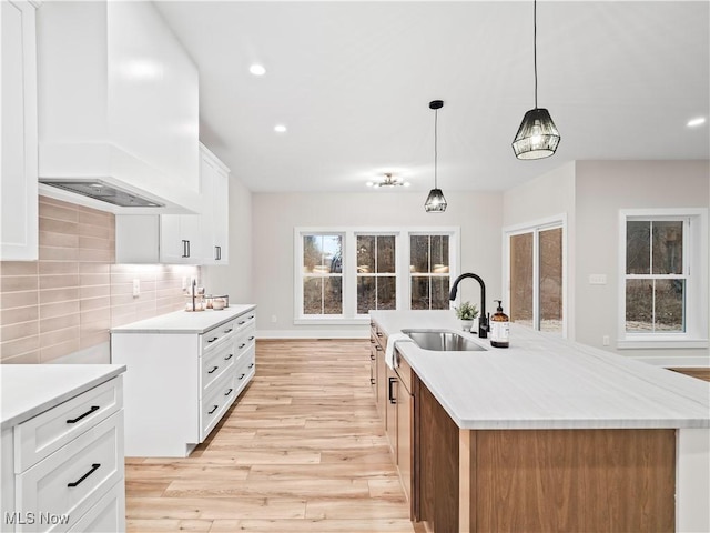 kitchen with white cabinets, decorative light fixtures, light hardwood / wood-style floors, and a kitchen island with sink