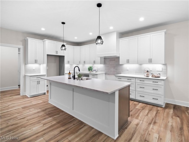 kitchen with backsplash, sink, light hardwood / wood-style flooring, white cabinets, and an island with sink