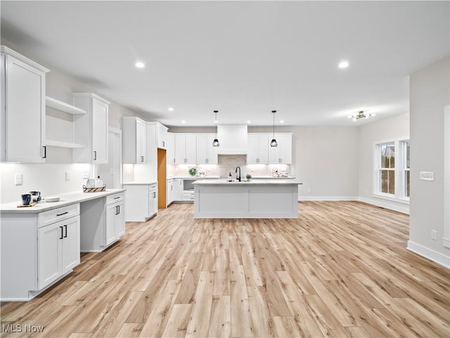 kitchen with pendant lighting, a kitchen island with sink, white cabinets, sink, and light hardwood / wood-style floors