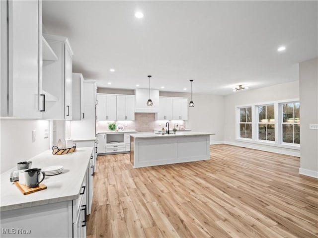 kitchen featuring sink, hanging light fixtures, an island with sink, white cabinets, and light wood-type flooring