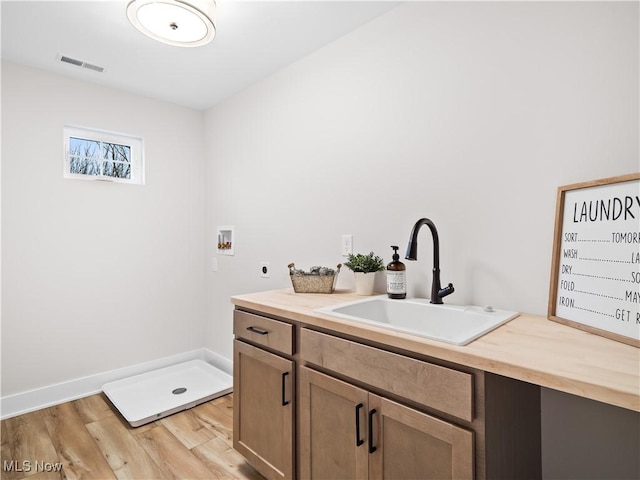 clothes washing area with cabinets, sink, washer hookup, hookup for an electric dryer, and light hardwood / wood-style floors