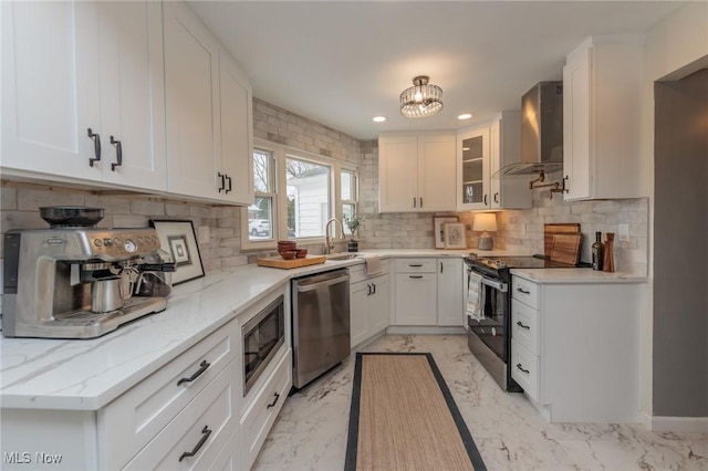 kitchen with appliances with stainless steel finishes, light stone counters, white cabinetry, and wall chimney range hood