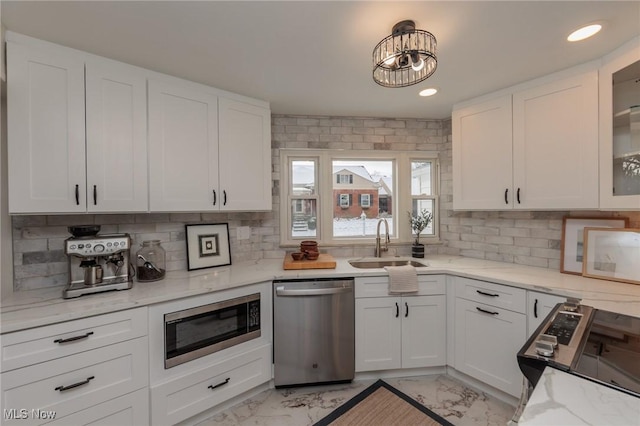 kitchen featuring appliances with stainless steel finishes, backsplash, light stone counters, sink, and white cabinets