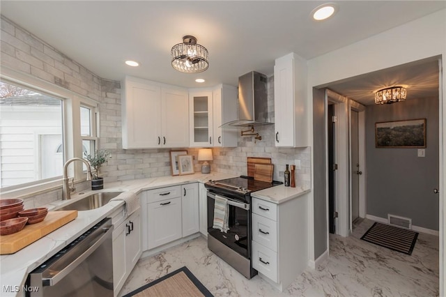 kitchen with light stone countertops, white cabinetry, sink, stainless steel appliances, and wall chimney range hood