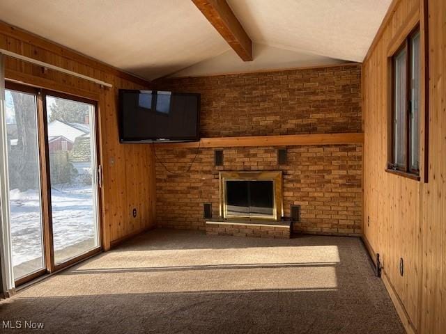 unfurnished living room featuring a brick fireplace, wooden walls, lofted ceiling with beams, and carpet