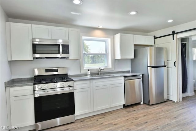 kitchen with a barn door, white cabinets, stainless steel appliances, and light wood-type flooring