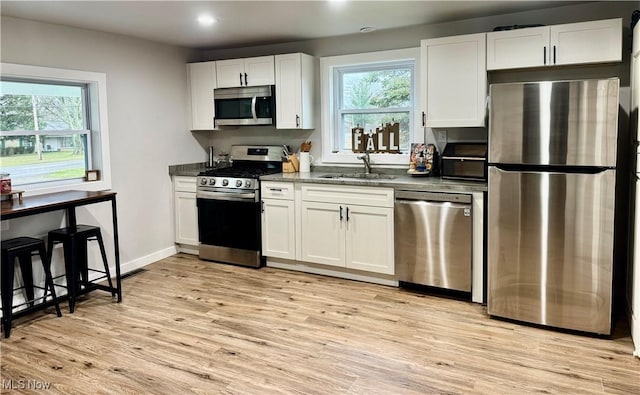 kitchen with stainless steel appliances, sink, dark stone countertops, white cabinets, and light hardwood / wood-style floors