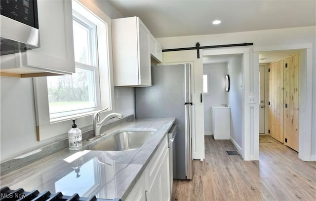 kitchen with white cabinets, light hardwood / wood-style flooring, light stone countertops, and a healthy amount of sunlight