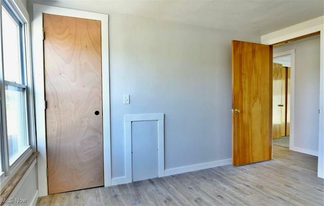 unfurnished bedroom with a closet, light wood-type flooring, and multiple windows