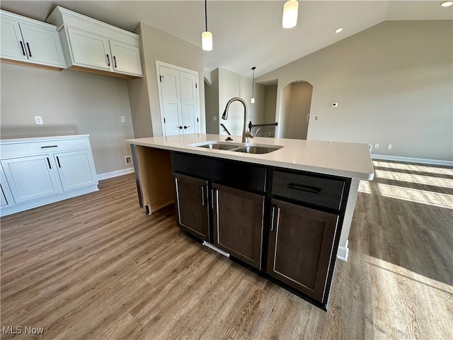 kitchen with light wood-type flooring, a kitchen island with sink, sink, hanging light fixtures, and lofted ceiling