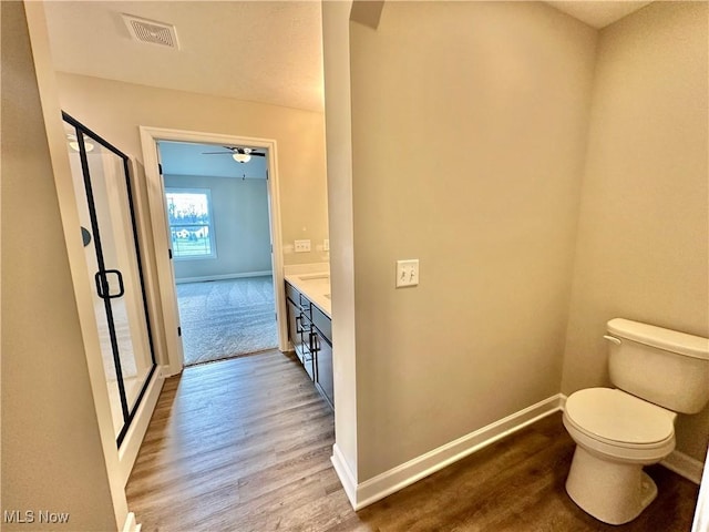 bathroom with ceiling fan, an enclosed shower, toilet, vanity, and hardwood / wood-style flooring