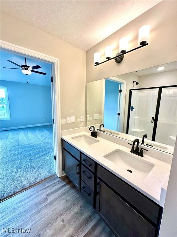 bathroom with walk in shower, vanity, a textured ceiling, ceiling fan, and wood-type flooring