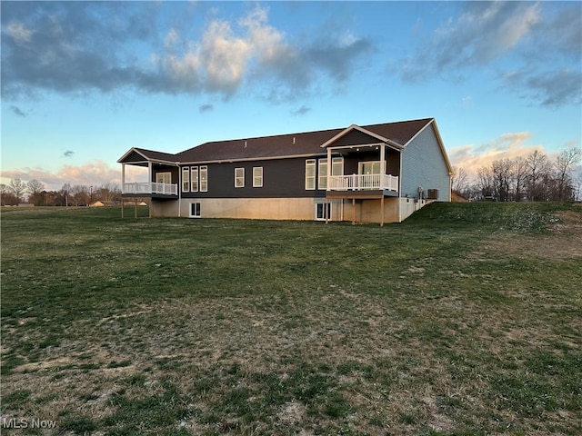 back house at dusk featuring a yard and a balcony