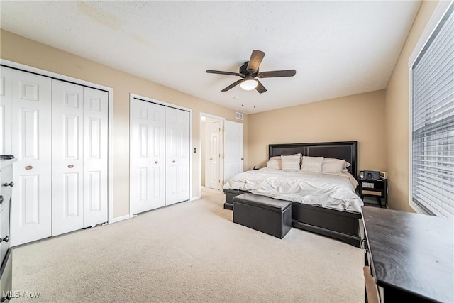 carpeted bedroom featuring multiple closets and ceiling fan