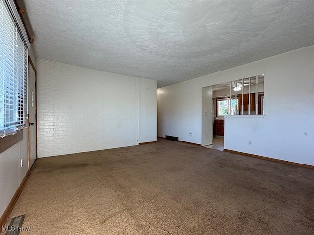 carpeted empty room featuring a textured ceiling and brick wall