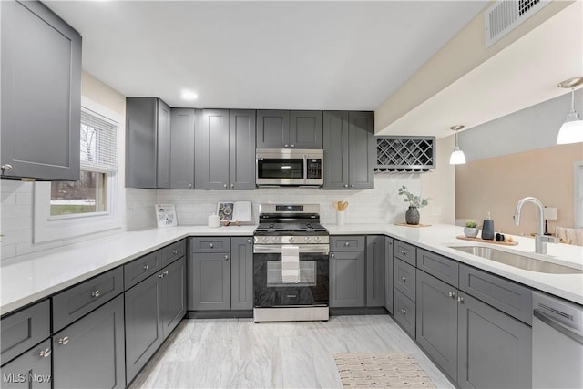 kitchen featuring sink, gray cabinetry, backsplash, stainless steel appliances, and decorative light fixtures