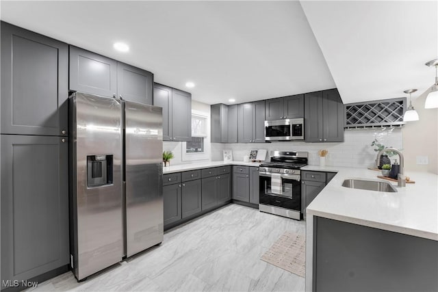 kitchen featuring appliances with stainless steel finishes, sink, gray cabinetry, decorative backsplash, and hanging light fixtures