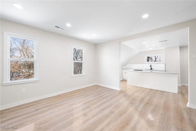 unfurnished living room featuring a wealth of natural light, sink, and light wood-type flooring