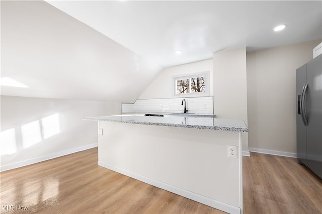 kitchen with lofted ceiling, light hardwood / wood-style flooring, stainless steel fridge, light stone countertops, and tasteful backsplash