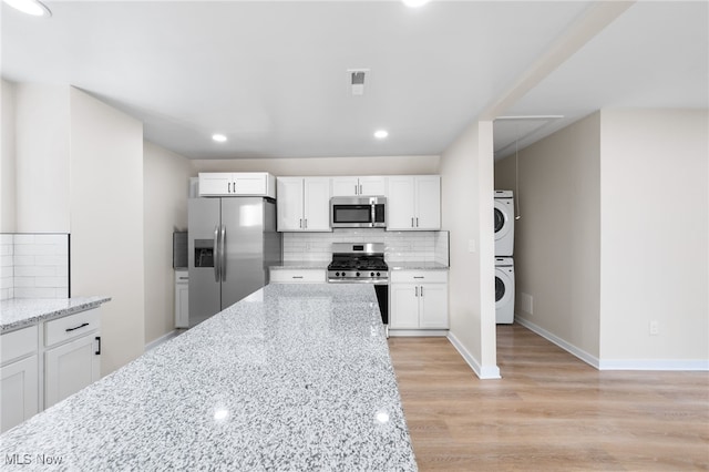 kitchen with white cabinets, light stone counters, stacked washing maching and dryer, and appliances with stainless steel finishes