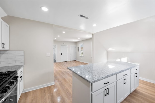 kitchen featuring light stone counters, light hardwood / wood-style floors, vaulted ceiling, black range, and white cabinets