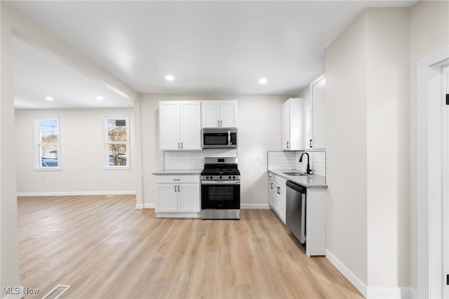 kitchen with backsplash, stainless steel appliances, sink, light hardwood / wood-style floors, and white cabinetry