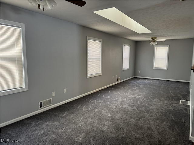 carpeted spare room with ceiling fan, a textured ceiling, and a skylight