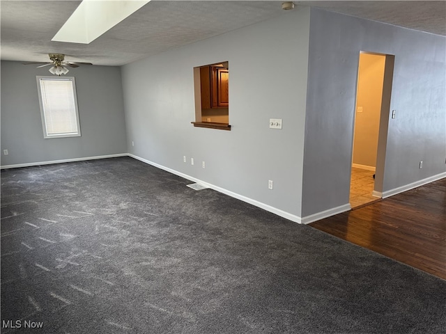 empty room featuring dark hardwood / wood-style floors, ceiling fan, a textured ceiling, and a skylight