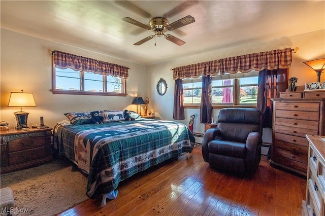 bedroom featuring dark hardwood / wood-style flooring, multiple windows, a baseboard heating unit, and ceiling fan