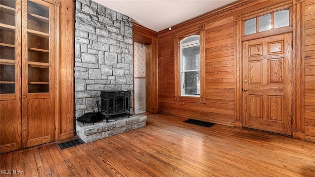 unfurnished living room with hardwood / wood-style floors, wood walls, and a wood stove