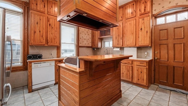 kitchen featuring dishwasher, light tile patterned floors, a wealth of natural light, and custom exhaust hood