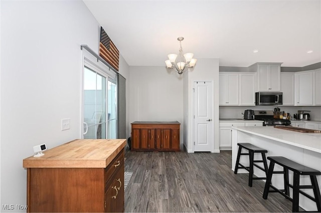 kitchen with dark wood-type flooring, a chandelier, appliances with stainless steel finishes, a kitchen breakfast bar, and white cabinets