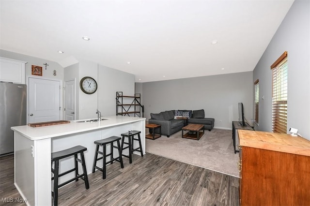 kitchen featuring dark hardwood / wood-style floors, stainless steel refrigerator, sink, a breakfast bar area, and a center island with sink