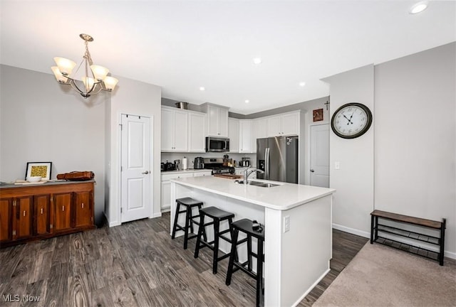 kitchen featuring hanging light fixtures, stainless steel appliances, white cabinets, a center island with sink, and dark hardwood / wood-style flooring