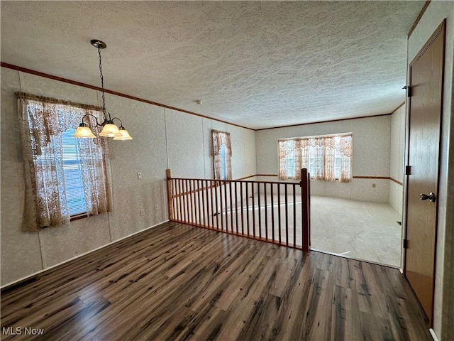 empty room featuring a chandelier, a textured ceiling, crown molding, and dark wood-type flooring