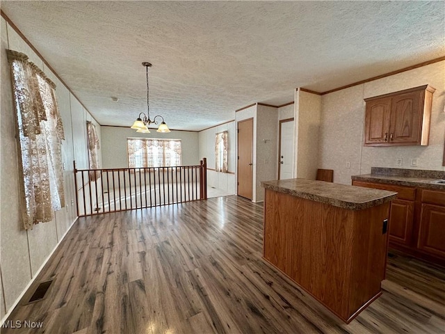 kitchen with an inviting chandelier, dark hardwood / wood-style floors, crown molding, a textured ceiling, and a kitchen island