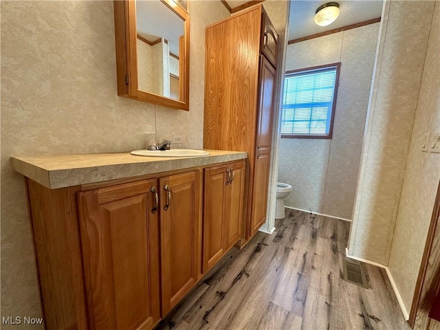 bathroom featuring toilet, vanity, wood-type flooring, and ornamental molding