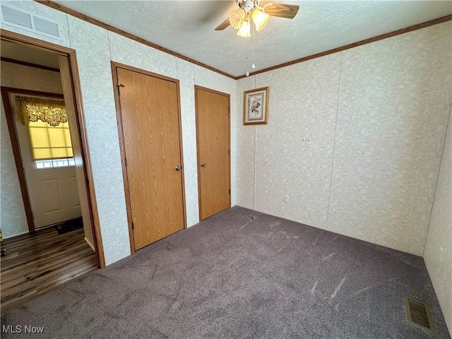 unfurnished bedroom with crown molding, ceiling fan, a textured ceiling, carpet floors, and multiple closets