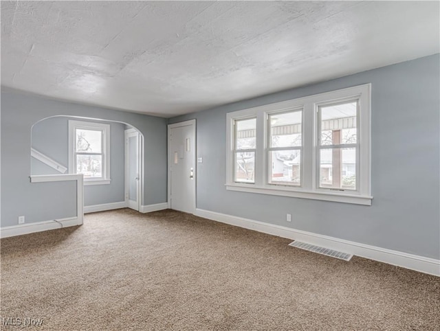 empty room with visible vents, arched walkways, baseboards, and carpet flooring