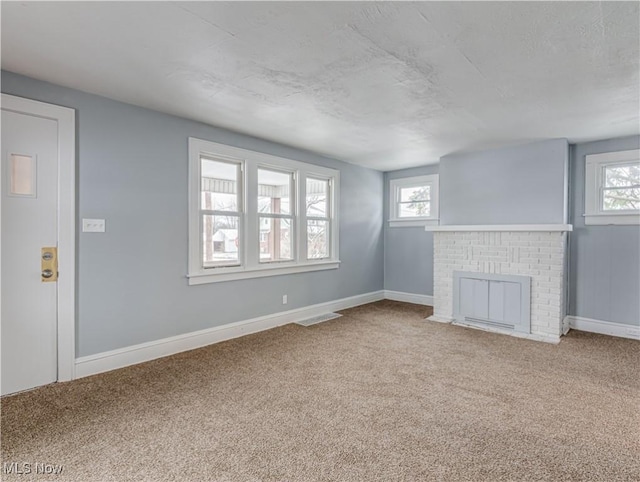 unfurnished living room with baseboards, a brick fireplace, a healthy amount of sunlight, and carpet flooring